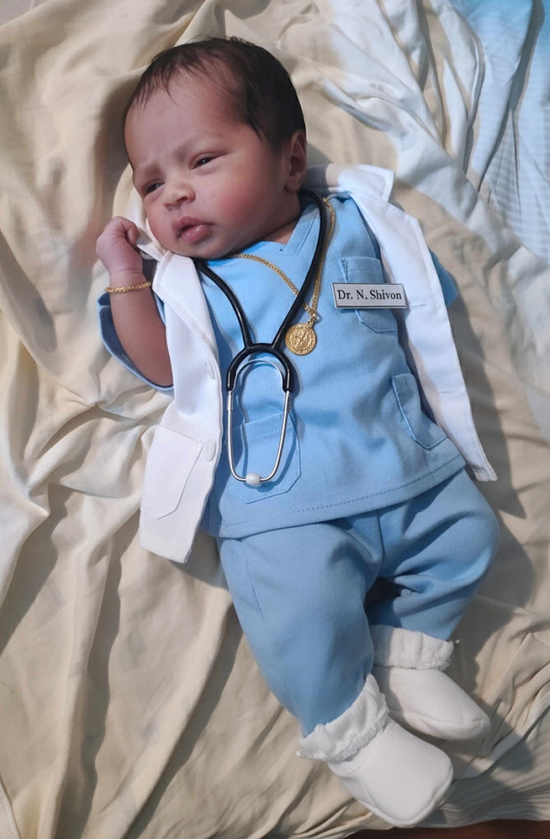 Shivon joined the competition — help win amazing prizes! baby, infant, doctor_costume, stethoscope, blue_clothing, white_coat, bracelet, necklace, footwear, lying_down, bed, blanket, cute, portrait, young_child, indoors, person, medical, newborn, soft_lighting