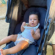 Lenaëlle participe au concours pour gagner de l'argent avec cette photo : baby, child, stroller, curly_hair, white_outfit, outdoor, playful, legs, face, expression, seat, comfort, sunlight, person, infant, cute, summer, relaxing, hands, young