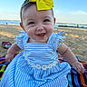 baby, child, smiling, yellow_bow, blue_dress, striped_dress, daisy_decor, beach, sand, sea, sky, blanket, happy, outdoor, sunlight, portrait, infant, sitting, cute, headband