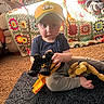 toddler, child, toy, construction_vehicle, action_figure, yellow_cap, crocheted_blanket, couch, rug, carpet, indoor, play, sitting, foot, clothing, person, sunlight, living_room, home, casual