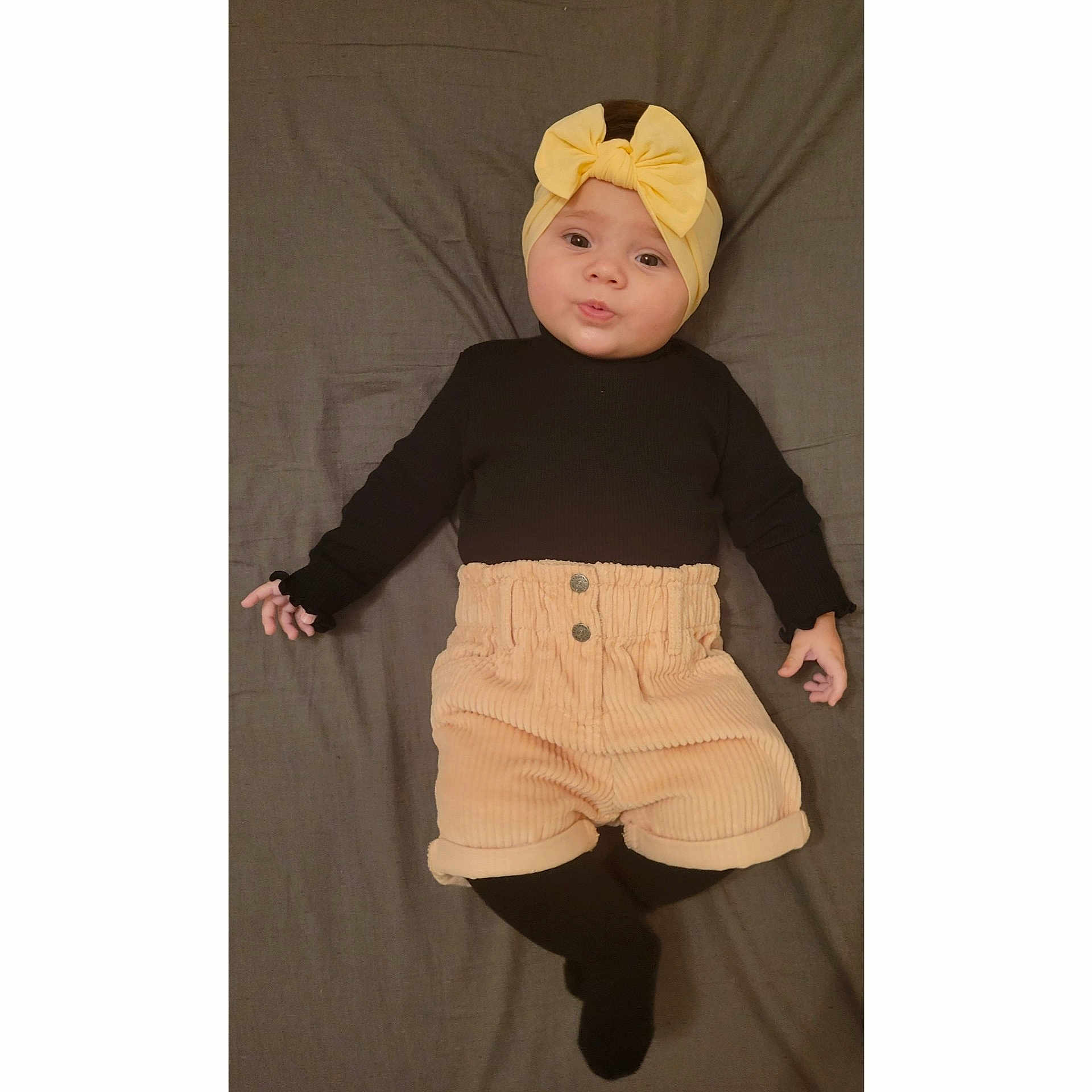 Jade a rejoint le concours — aidez-le/la à gagner de superbes lots ! baby, child, infant, headband, yellow_bow, black_shirt, beige_shorts, corduroy, black_tights, pouty_face, lying_down, blanket, indoor, cute, fashion, portrait, smile, hands, feet, person