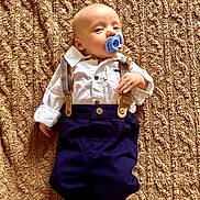 Monroe is registered to the contest to win money with this photo: baby, blanket, child, clothing, cute, expression, face, foot, hand, head, indoors, infant, lying_down, navy_pants, pacifier, portrait, suspenders, texture, white_shirt, young
