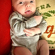 Monroe is registered to the contest to win money with this photo: baby, infant, face, tongue, onesie, clothing, cushion, pillow, holiday, indoor, cute, skin, person, expression, red, grey, comfort, lying, closeup, child