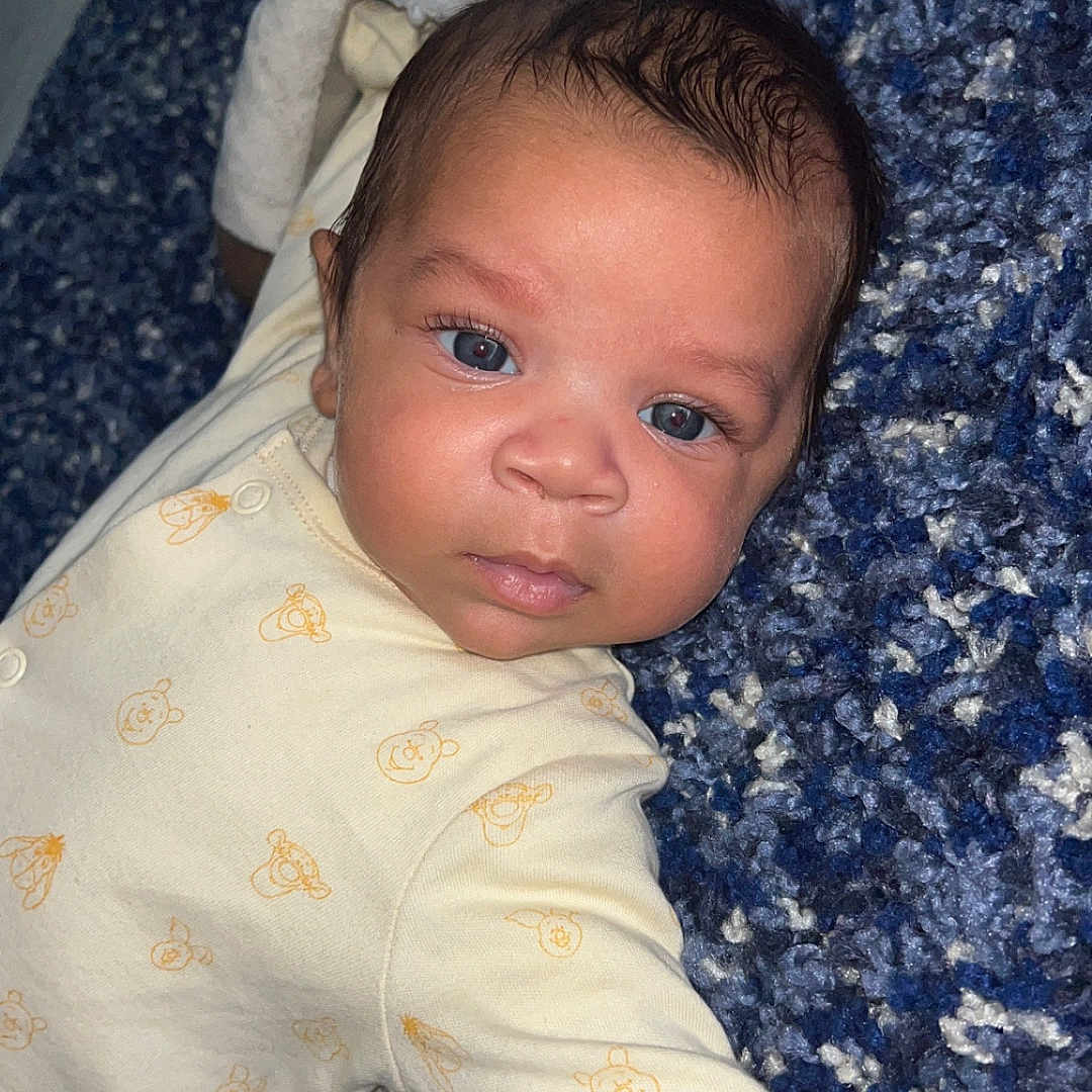 Cairo-Cruz joined the competition — help win amazing prizes! baby, blue_eyes, carpet, child, clothing, curious, cute, expression, face, head, indoors, infant, lying_down, onesie, pattern, person, skin, soft, textured, young