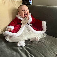 Rosalie-Marie is registered to the contest to win money with this photo: baby, chewing, child, clothing_tag, couch, curious, cute, dress, festive, holiday, home, indoor, infant, joyful, person, red_dress, sitting, smiling, white_fur_trim, white_socks