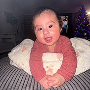 Sofia is registered to the contest to win money with this photo: baby, child, smiling, blanket, cozy, indoor, christmas_tree, holiday, soft_texture, couch, happy, portrait, infant, clothing, person, furniture, decor, warm_lighting, face, home
