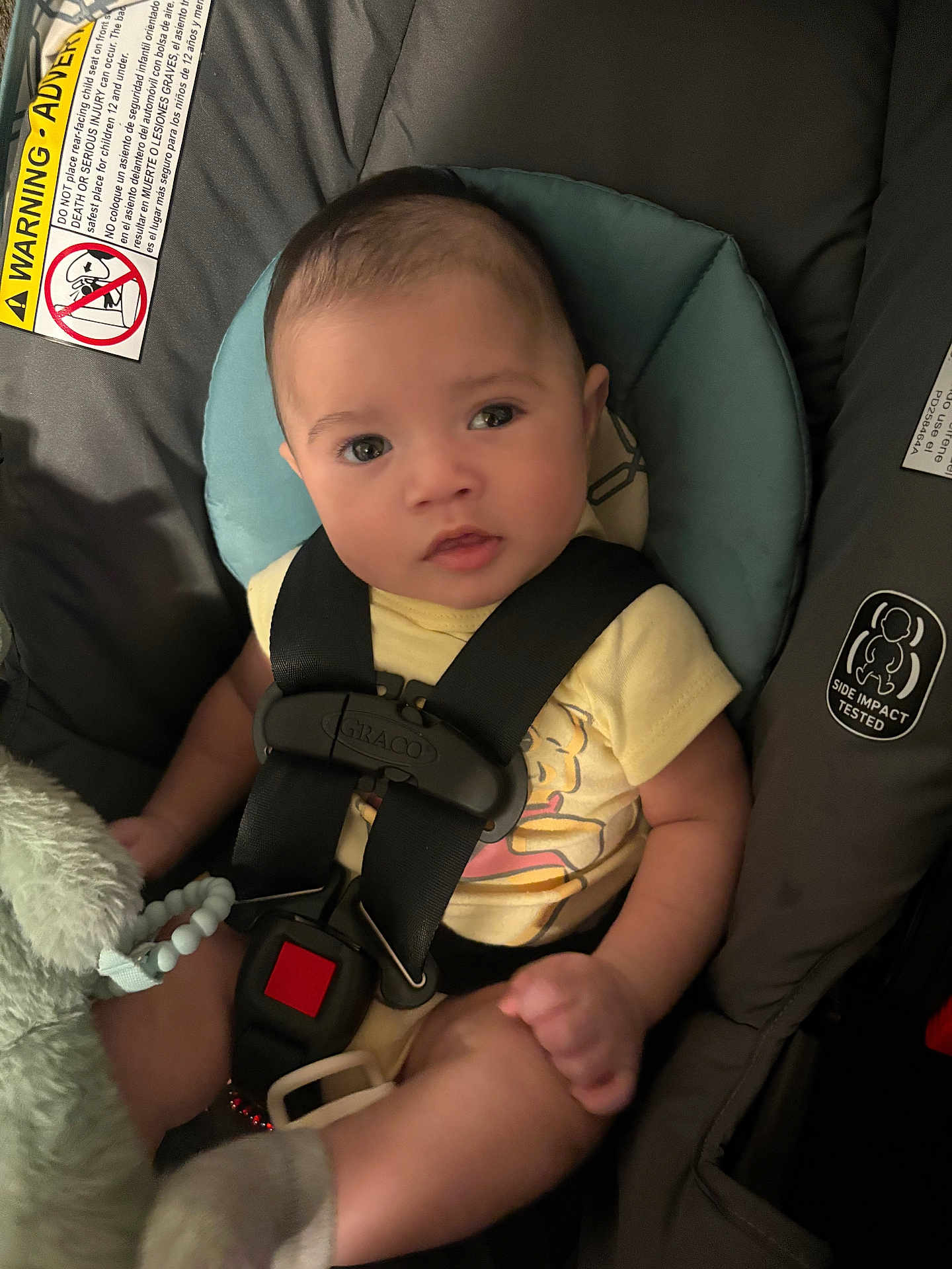 Naveen is registered to the contest to win money with this photo: baby, car_seat, child, infant, straps, yellow_shirt, plush_toy, socks, face, eyes, hand, leg, seatbelt, graco, cushion, indoor, portrait, cute, sitting, soft_lighting