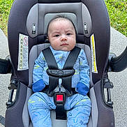 Russel is registered to the contest to win money with this photo: baby, infant, car_seat, blue_onesie, shark_pattern, sitting, straps, outdoor, grass, concrete, serious_expression, child, clothing, footed_pajamas, safety_harness, person, head, face, cute, young_child