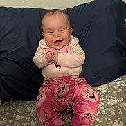Sophia is registered to the contest to win money with this photo: baby, child, smiling, pink_pants, happy_faces, bed, pillow, blue_pillow, floral_bedspread, clothing, socks, cute, infant, indoors, person, portrait, hands, sitting, wall, joyful
