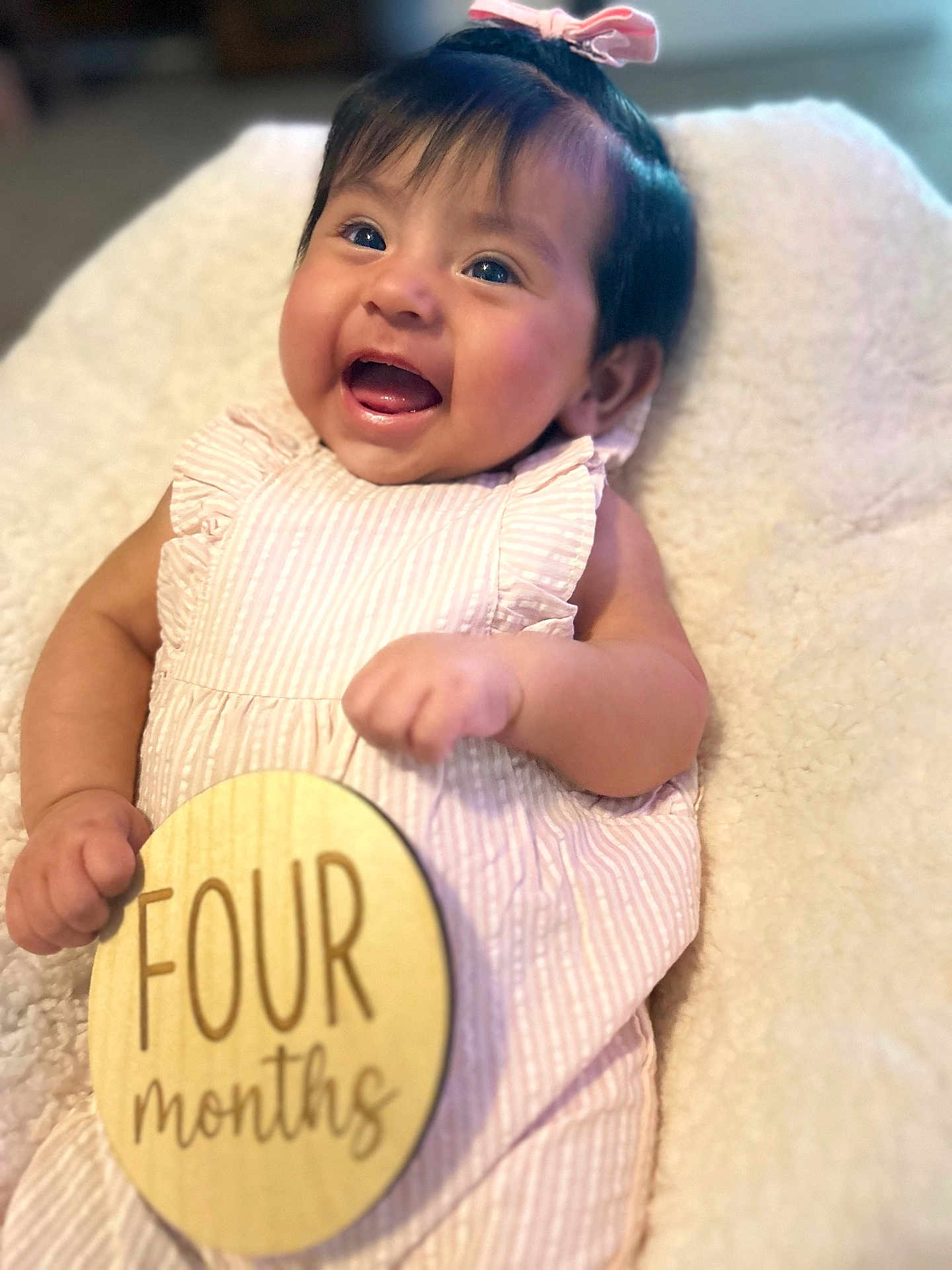 Camila is registered to the contest to win money with this photo: baby, infant, smiling, happy, pink_bow, striped_dress, wooden_sign, four_months, cute, portrait, child, soft_blanket, lying_down, hand, face, cheerful, indoors, closeup, young, adorable