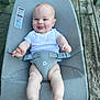 baby, child, infant, smiling, tongue_out, white_clothing, baby_seat, mesh_fabric, straps, wooden_deck, outdoor, cute, happy, skin, legs, feet, playful, seat, person, portrait