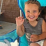 Cash joined the competition — help win amazing prizes! child, toddler, smiling, braided_hair, green_hair_ties, blue_chair, waving_hand, tank_top, outdoor, concrete_floor, brick_wall, happy, cute, person, seated, summer, playful, young_child, casual_clothing, portrait