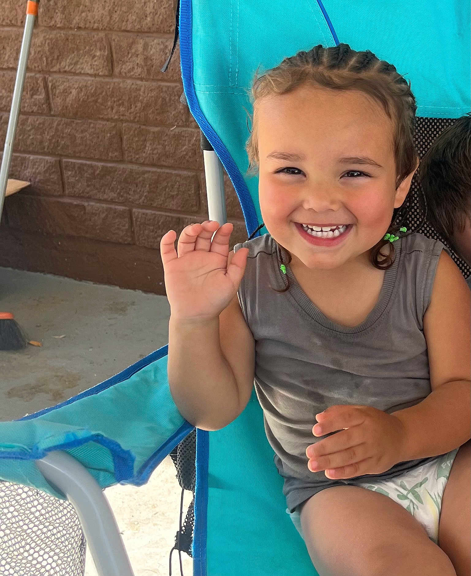 Cash joined the competition — help win amazing prizes! child, toddler, smiling, braided_hair, green_hair_ties, blue_chair, waving_hand, tank_top, outdoor, concrete_floor, brick_wall, happy, cute, person, seated, summer, playful, young_child, casual_clothing, portrait