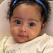 Brylee joined the competition — help win amazing prizes! baby, infant, headband, blue_bow, big_eyes, curly_hair, onesie, princess_text, blanket, quilted_background, portrait, closeup, cheeks, eyelashes, smile, bedding, cute, human_face, sitting, soft_lighting