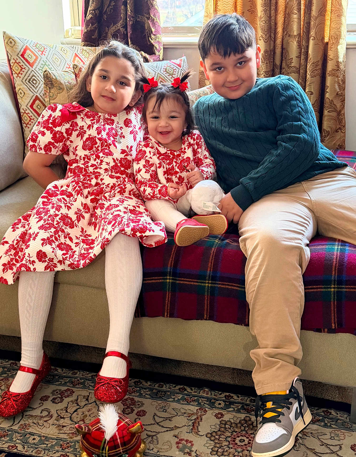 Atarah is registered to the contest to win money with this photo: child, children, sitting, couch, indoor, smiling, family, red_dress, floral_pattern, tights, shoes, window, curtains, carpet, toy, happy, siblings, portrait, home, casual_clothing