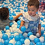 child, toddler, ball_pit, blue_balls, white_balls, playing, curly_hair, short_hair, overalls, stitch_character, indoor, fun, happy, cute, kids, toys, plastic_balls, play_area, colorful, smiling