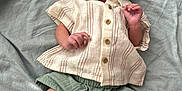 Khalil is registered to the contest to win money with this photo: baby, infant, clothing, shirt, shorts, sneakers, lying_down, blanket, expression, curious, young_child, footwear, fabric, texture, person, cute, small, indoors, casual, newborn