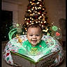 baby, child, smiling, christmas_tree, holiday, christmas_lights, book, reading, grinch, festive, pillow, indoors, magic_effects, cartoon, green_clothing, cute, holiday_decor, celebration, portrait, happy