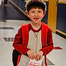 backpack, boy, casual_wear, child, donuts, food, fun, happy, holding, indoor, person, portrait, red_clothing, school_hallway, smiling, snack, tooth_gap, visors, waiting, young