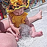 baby, barefoot, child, colorful, curious, fountain, fun, legs, netting, outdoor, person, play_area, sitting, summer, sunflower_pattern, toddler, water, water_play, yellow_hat, yellow_swimsuit