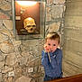 Esteban participe au concours pour gagner de l'argent avec cette photo : child, boy, stick, blue_sweater, stone_wall, museum, skull, display_case, glass, lighting, curious, standing, indoor, plaster_skull, casual_clothing, young, playful, wall_outlet, exhibit, portrait