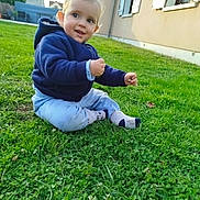 Rafael a rejoint le concours — aidez-le/la à gagner de superbes lots ! toddler, child, grass, outdoor, smile, blue_hoodie, pants, socks, house, window, shutters, greenery, nature, young_child, baby, sitting, curious, daylight, casual_clothing, suburb