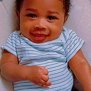 Sincere is registered to the contest to win money with this photo: baby, child, infant, smiling, happy, portrait, close_up, curly_hair, striped_onesie, blue_clothing, lying_down, bed, pillow, nursery, indoor, face, eyes, hands, adorable, photography