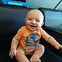 Archer is registered to the contest to win money with this photo: baby, child, smiling, orange_shirt, sitting, black_chair, tablet, indoor, happy, cute, skin, head, legs, feet, arms, cactus_design, sun_design, person, infant, casual