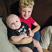 Lakestine joined the competition — help win amazing prizes! baby, child, smile, couch, curly_hair, blond_hair, black_clothing, red_shirt, sitting, indoor, holding, person, infant, happy, portrait, family, cute, skin, face, eyes