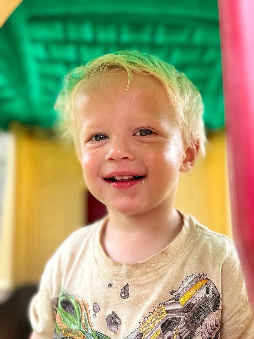 Tobias joined the competition — help win amazing prizes! child, toddler, blonde_hair, smiling, drool, tshirt, graphic_tee, portrait, face, happy, young_child, casual_clothing, indoors, colorful_background, closeup, cute, person, head_and_shoulders, bright_colors, soft_focus