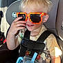 toddler, child, car_seat, sunglasses, blonde_hair, sippy_cup, seatbelt, casual_clothing, car_interior, sunlight, hand, smile, shorts, tshirt, plastic, travel, daylight, cute, young_child, portrait