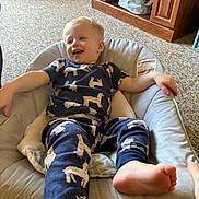Tobias joined the competition — help win amazing prizes! toddler, child, baby_seat, pajamas, llama_print, carpet, wooden_furniture, cushion, indoor, smiling, barefoot, relaxed, home, furniture, person, clothing, seat, happy, infant, cute