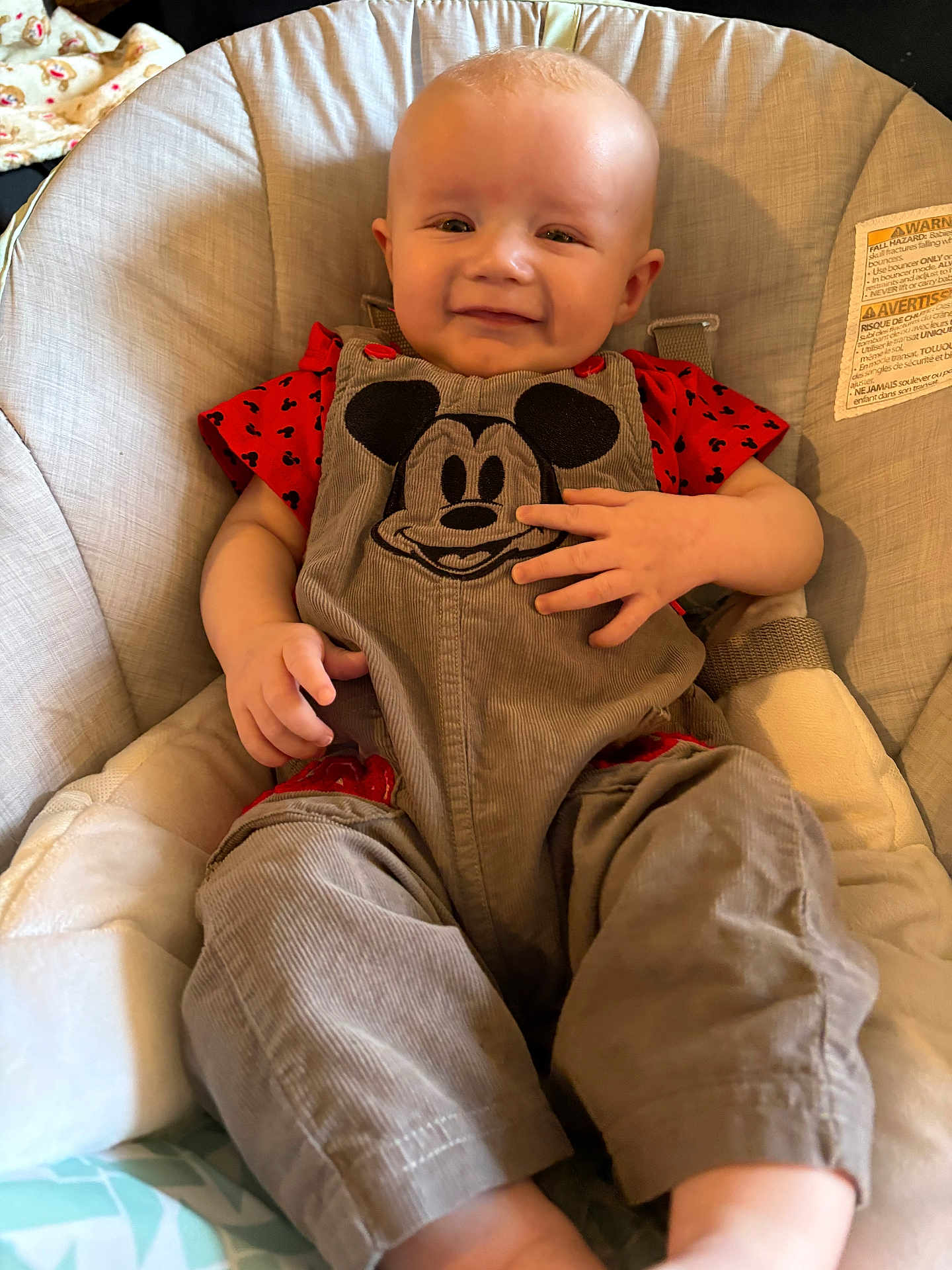 Bradlee is registered to the contest to win money with this photo: baby, child, smiling, overalls, mickey_mouse, red_shirt, baby_chair, cushion, comfortable, indoor, infant, cute, portrait, clothing, happy, hand, face, seat, soft, baby_furniture