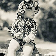 Nyah is registered to the contest to win money with this photo: baby, black_and_white, blocks, bonnet, child, clothing, concrete, curious, cute, daylight, hat, holding, leopard_print, outdoor, person, portrait, sitting, stick, toddler, young_child