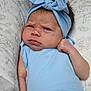 baby, infant, blue_headband, blue_onesie, face, expression, cushion, pattern, closeup, skin, hair, newborn, indoor, person, cute, child, portrait, resting, fist, headwear