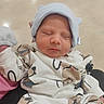 newborn, baby, infant, sleeping, portrait, face, hat, knit_hat, clothing, onesie, blanket, bundled, peaceful, indoors, close_up, sitting, caregiver, patterned, soft_lighting, photography