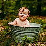 Sawyer is registered to the contest to win money with this photo: baby, child, metal_bucket, outdoor, forest, greenery, leaves, grass, nature, toddler, curious, bare_chest, smiling, cute, portrait, young_child, sitting, daylight, playful, rustic