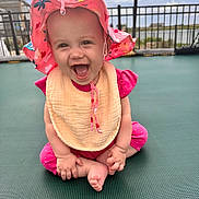 Mary joined the competition — help win amazing prizes! baby, child, smiling, happy, pink_clothing, sun_hat, outdoor, trampoline, fence, playful, cute, sitting, infant, young_child, joy, fun, summer, daylight, expression, portrait
