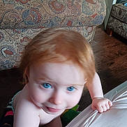 Presley is registered to the contest to win money with this photo: toddler, child, red_hair, blue_eyes, indoor, couch, patterned_fabric, wooden_floor, hand, grip, curious, skin, bare_shoulders, home, carpet, person, furniture, blur, closeup, expression