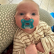 Maël participe au concours pour gagner de l'argent avec cette photo : baby, pacifier, blue_eyes, striped_pajamas, cushion, indoor, tile_floor, infant, closeup, child, person, cozy, cute, comfort, hands, face, expression, looking_up, soft_light, home