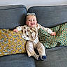 baby, bib, child, corduroy_pants, couch, cozy, fabric_texture, happy, home_interior, infant, patterned_pillow, pillow, playful, portrait, sitting, smiling, socks, striped_socks, sunglasses, wall