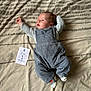 baby, infant, bed, blanket, clothing, overalls, socks, face, person, lying_down, newborn, one_month, card, pattern, striped_socks, cute, small, indoors, resting, celebration