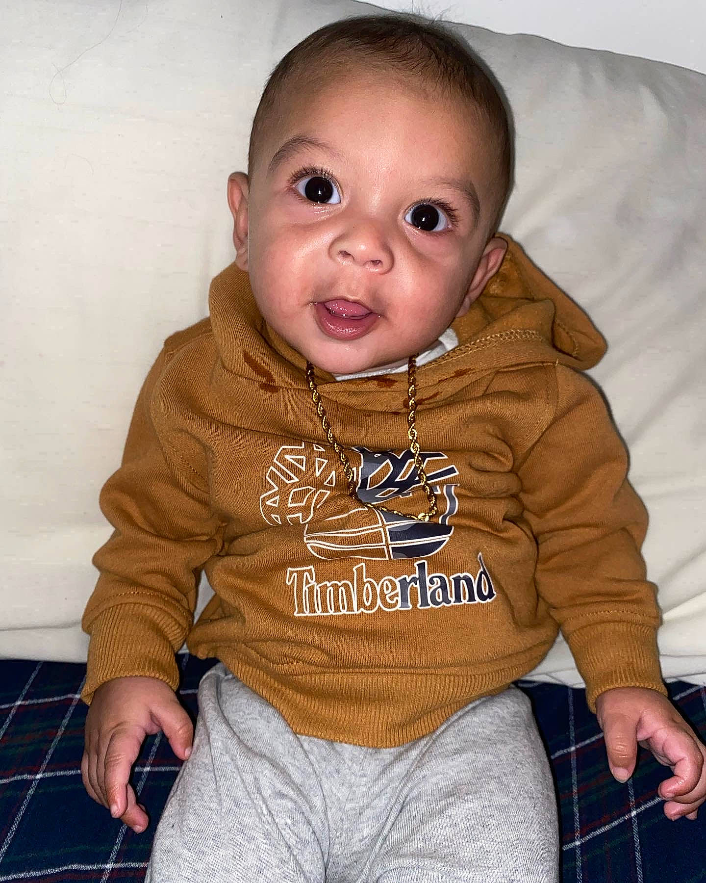 Jamal is registered to the contest to win money with this photo: baby, baby_toddler_clothing, cheek, child, collar, comfort, fur, happy, hood, human_body, long_sleeved_t_shirt, neck, pattern, person, pink, plaid, sitting, sleeve, t_shirt, tartan