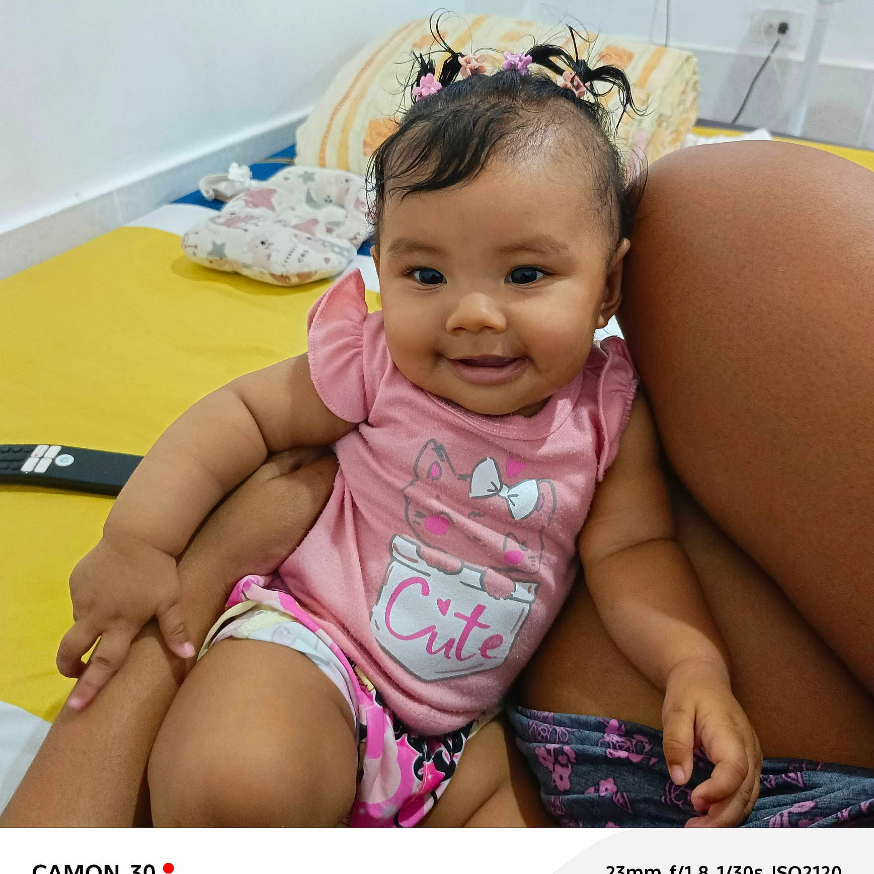 Emma Barreto joined the competition — help win amazing prizes! baby, bed, casual_clothing, child, closeup, cute, hair_clips, hand, happy, indoor, infant, legs, person, pillow, pink_shirt, portrait, remote_control, sitting, skin, smiling