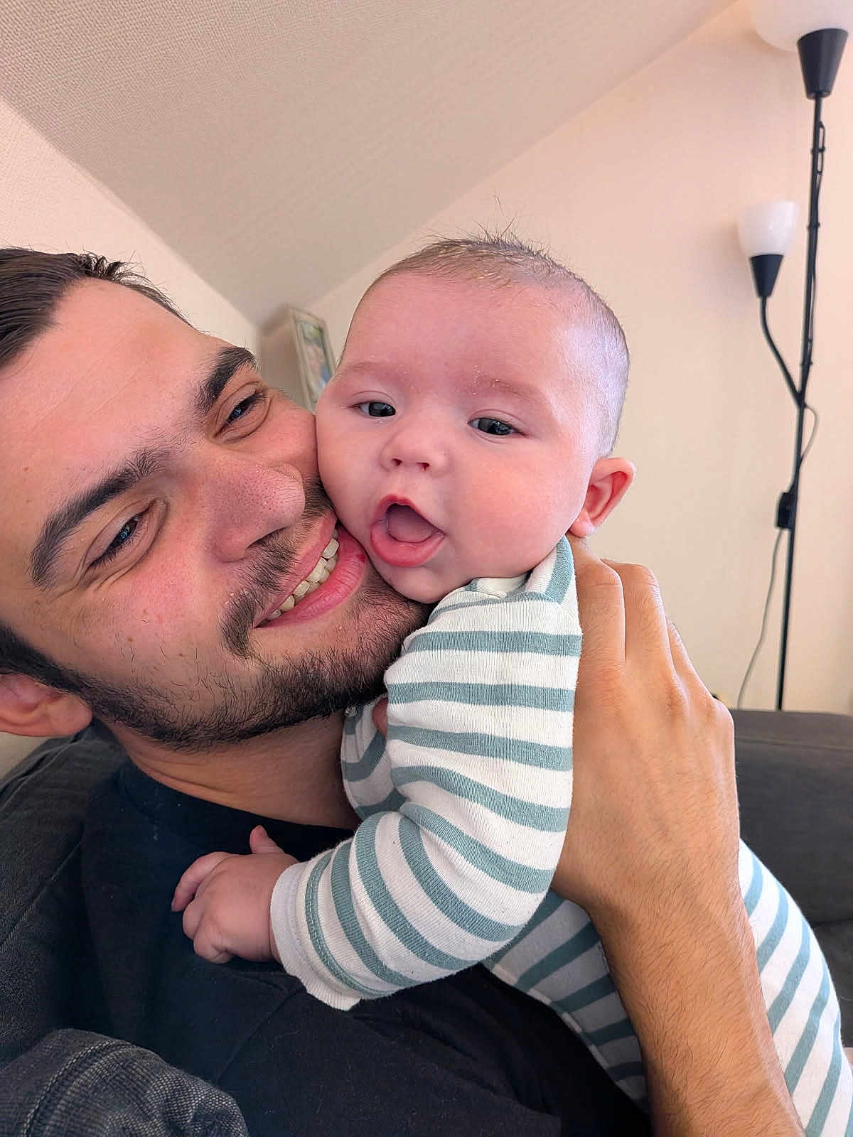 Elio participe au concours pour gagner de l'argent avec cette photo : baby, man, smiling, hug, indoor, striped_clothing, facial_hair, couch, hand, portrait, happy, family, parent, child, cozy, lamp, living_room, close_up, skin, casual