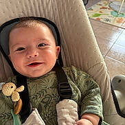 Elio a rejoint le concours — aidez-le/la à gagner de superbes lots ! baby, smiling, indoor, baby_seat, harness, toy, crocheted_toy, green_outfit, patterned_clothing, hand, face, cushion, seat, floor_tiles, play_mat, child, infant, cute, happy, person