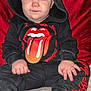 toddler, child, hoodie, black_clothing, rolling_stones_logo, sitting, red_cushion, pink_socks, indoor, curious_expression, face, hands, feet, soft_surface, casual_wear, portrait, baby, person, young_child, cozy