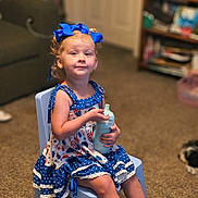 Serinaty is registered to the contest to win money with this photo: child, girl, sitting, blue_bow, dress, polka_dot, chair, sippy_cup, curly_hair, indoor, carpet, living_room, furniture, pet, dog, bookshelf, portrait, cute, smile, person