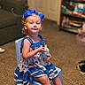 child, girl, sitting, blue_bow, dress, polka_dot, chair, sippy_cup, curly_hair, indoor, carpet, living_room, furniture, pet, dog, bookshelf, portrait, cute, smile, person