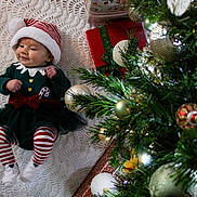 Poppy is registered to the contest to win money with this photo: baby, christmas, holiday, tree, ornaments, presents, blanket, festive, hat, striped, red, white, green, smile, cute, infant, clothing, celebration, decorations, toddler